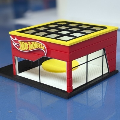 Loja miniatura Hot Wheels vermelha com teto amarelo e janelas de vidro.