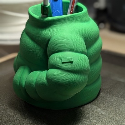 Organizador de secretária verde em forma de braço musculoso com canetas e fita adesiva