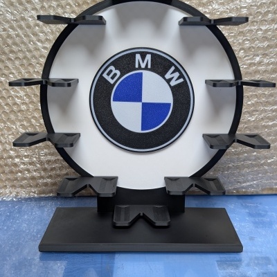 Suporte preto com logotipo BMW e ganchos, sobre superfície azul e fundo de plástico bolha