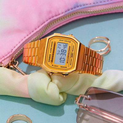 Relógio digital dourado CASIO sobre laço de tecido e bolsa rosa