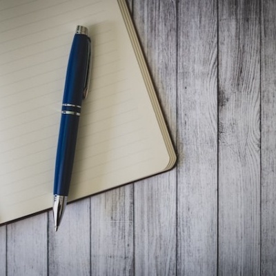 Caderno aberto com caneta azul sobre superfície de madeira cinza