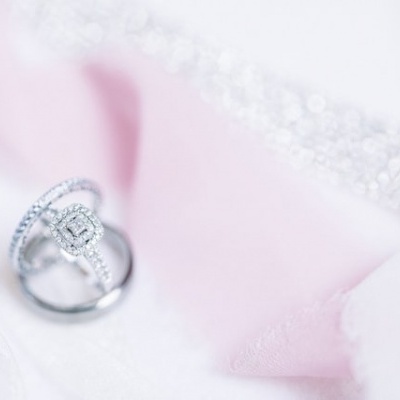 Anel prateado com pedras brilhantes sobre tecido rosa e branco.