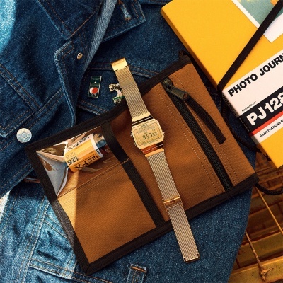 Relógio digital Casio dourado com bracelete metálica sobre bolsa castanha e casaco de ganga azul