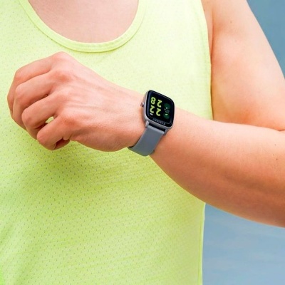 Relógio inteligente preto com bracelete cinzenta no pulso de pessoa com camisola amarela