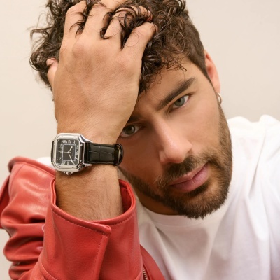 Relógio quadrado prateado com bracelete preta em pulso de homem