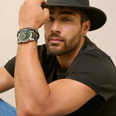 Homem com chapéu e t-shirt preta a usar relógio de pulso verde com pulseira preta