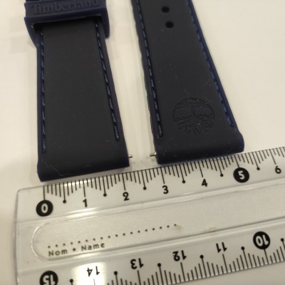 Correia de relógio preta com costura azul e logótipo Timberland junto a uma régua transparente