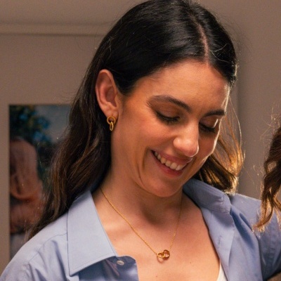 Mulher com cabelo castanho escuro, camisa azul clara e colar dourado