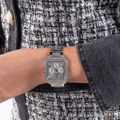 Relógio de pulso prateado com brilhantes em pulso de pessoa com casaco preto e padrão pied-de-poule