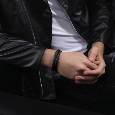 Pulseira preta trançada de couro no pulso de um homem com casaco preto de pele.