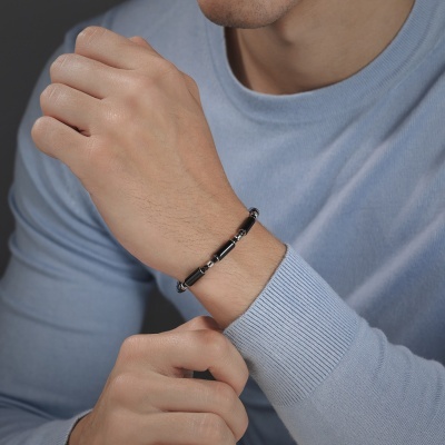 Pulseira masculina de metal prateado com elementos pretos no pulso de homem