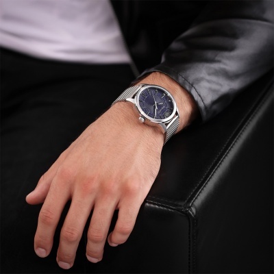 Relógio de pulso com bracelete metálica prateada e mostrador azul no pulso de uma pessoa