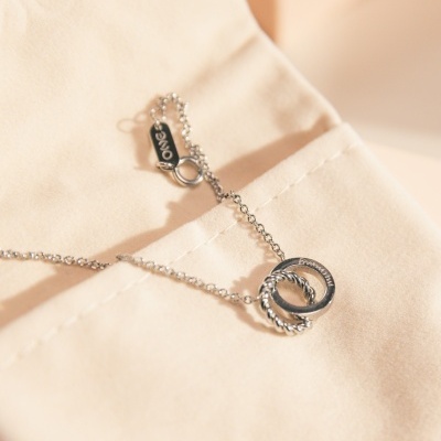 Colar prateado com anéis entrelaçados pendurados sobre tecido bege claro.