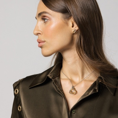 Colar dourado entrelaçado usado por mulher com blusa verde escuro e fundo cinza