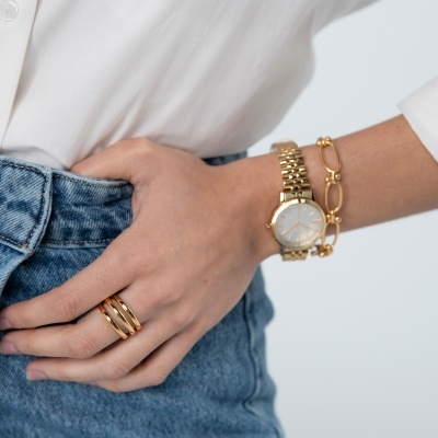 Relógio dourado com bracelete de elos metálicos e pulseira dourada no pulso de uma pessoa com camisa branca.