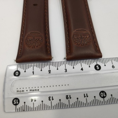 Dois elos de relógio castanhos em couro com logótipo, sobre régua transparente