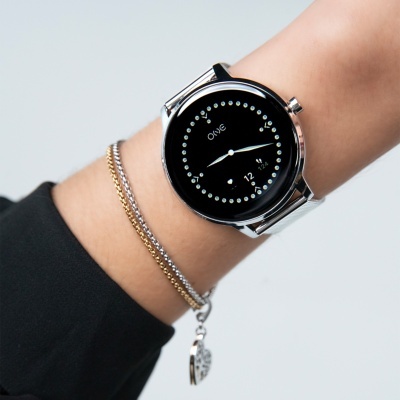 Relógio de pulso preto com pulseira metálica prateada e duas pulseiras finas ao lado