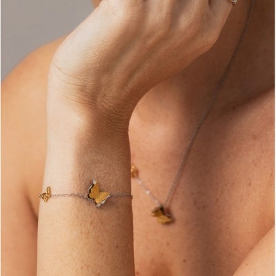 Pulseira e colar com borboletas douradas e prateadas em cadeia fina prateada no braço e pescoço de pessoa com pele clara