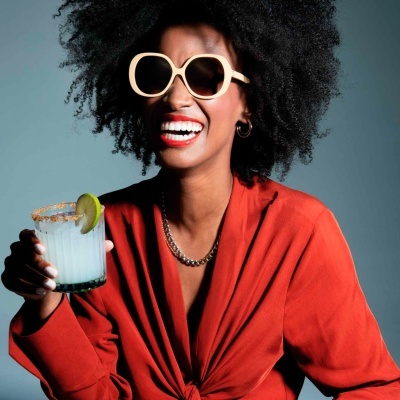 Mulher com óculos de sol a usar vestido vermelho a segurar copo de bebida branca com limão