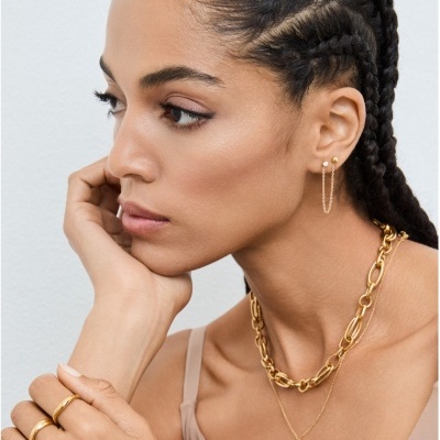 Mulher com brincos, anéis e colares dourados usando top bege.