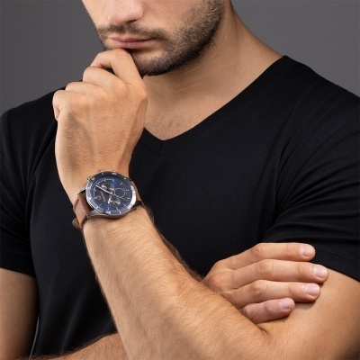 Relógio de pulso azul com pulseira de couro castanho num braço de homem com camisa preta