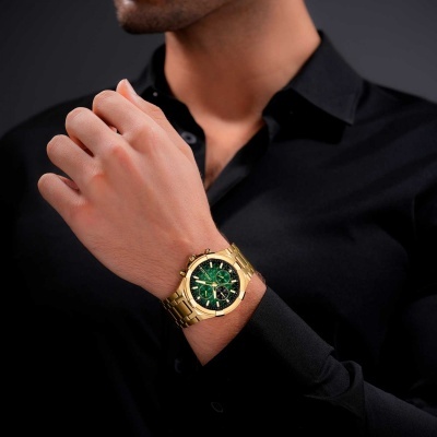 Relógio de pulso dourado com mostrador verde no pulso de um homem com camisa preta