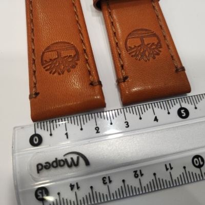 Dois segmentos de pulseira em pele castanha com gravação de logotipo e régua transparente em fundo branco