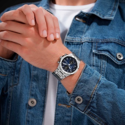 Relógio metálico prateado com mostrador azul em pulso com casaco de ganga azul.