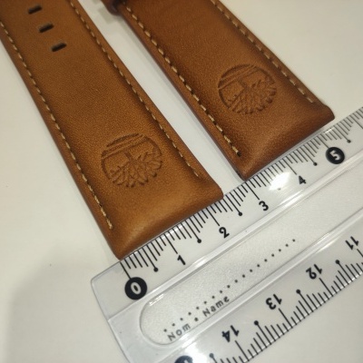 Correia de relógio em couro castanho com costura bege e gravação em relevo junto a régua transparente