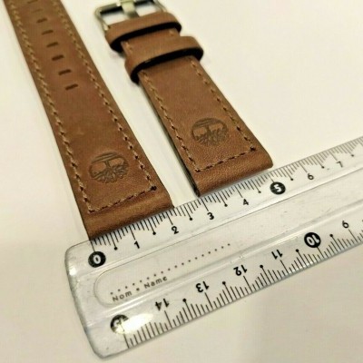 Duas pulseiras de relógio castanhas em pele com logótipo de árvore junto a uma régua transparente.
