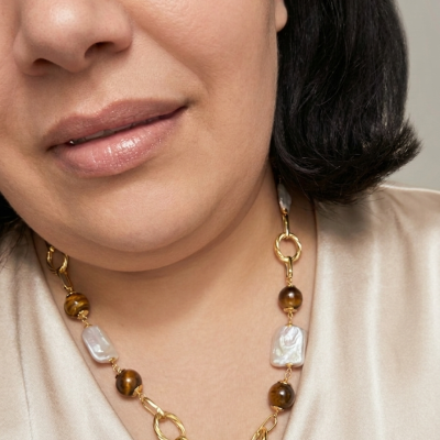 Colar dourado com pedras marrons e pérolas barrocas usado por mulher