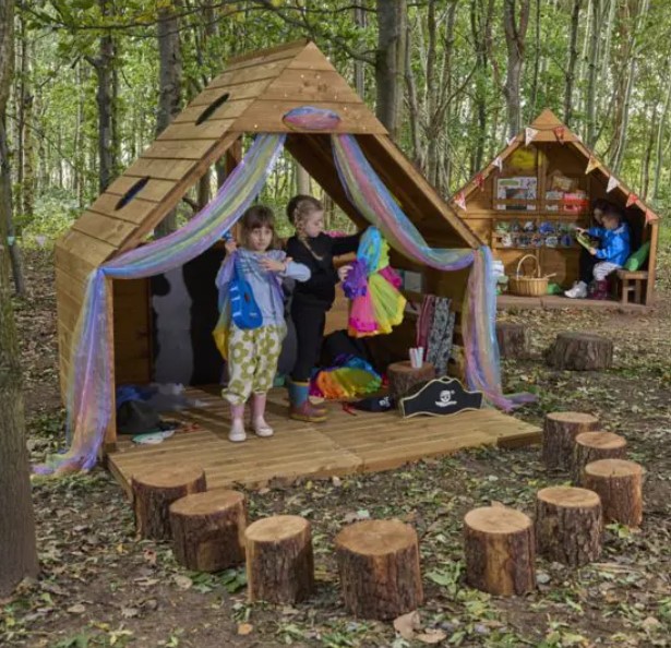 Espaço de Aprendizagem & Convívio - Learn & Lounge Forest Fern Casas de madeira para brincar com cortinas coloridas e troncos para sentar em ambiente natural