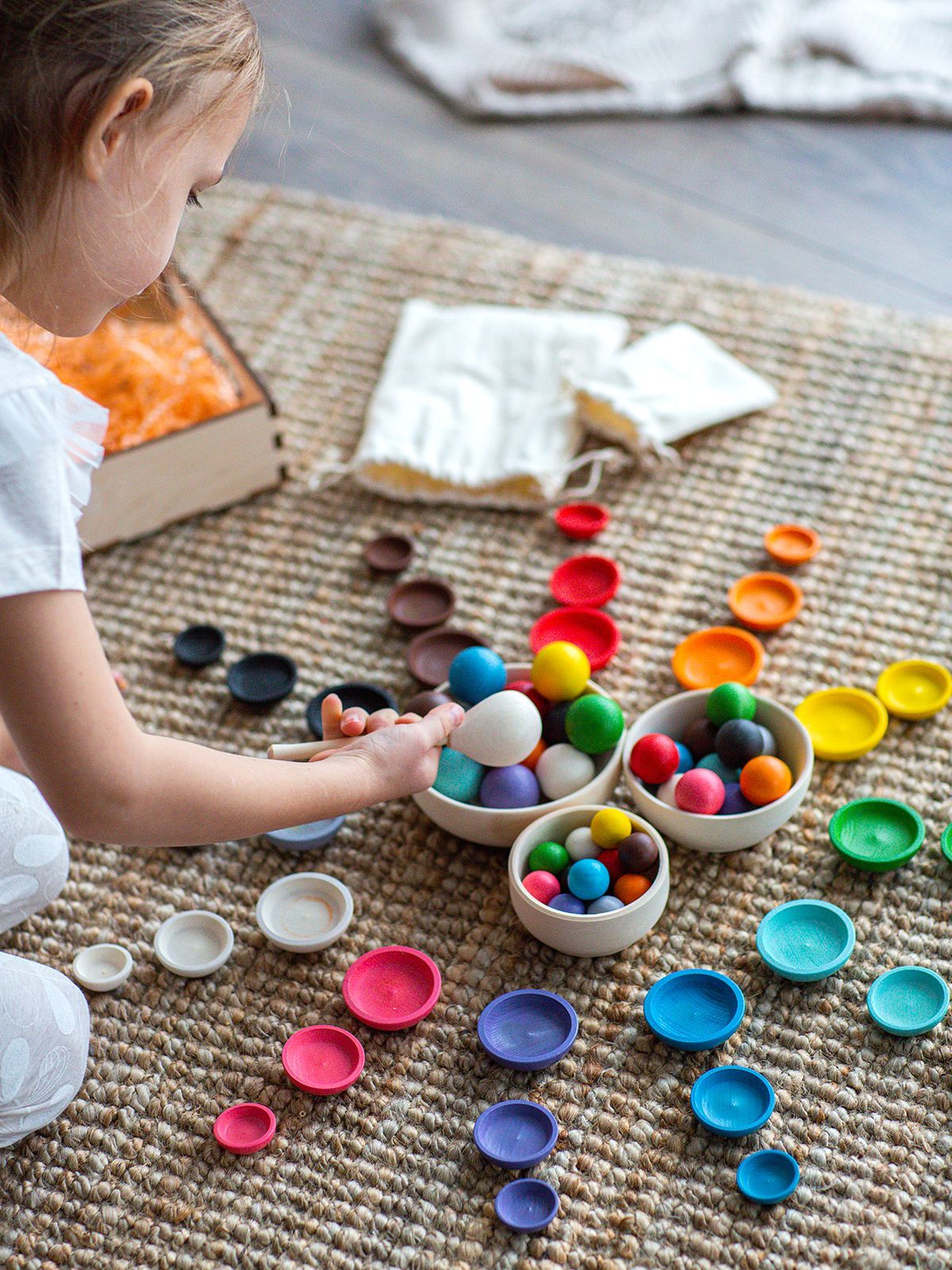 Box - Colors and sizes Criança a brincar com bolas e tampas coloridas em tapete bege