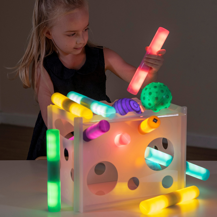 Torre suporte de acrílico translúcido Brinquedo interativo infantil com bastões coloridos luminosos e bola verde texturizada numa mesa com uma menina a brincar