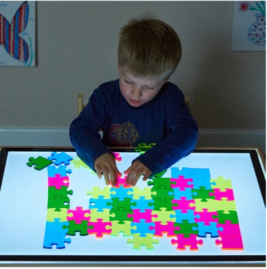 Puzzle Translúcido Criança a montar puzzle colorido numa superfície iluminada