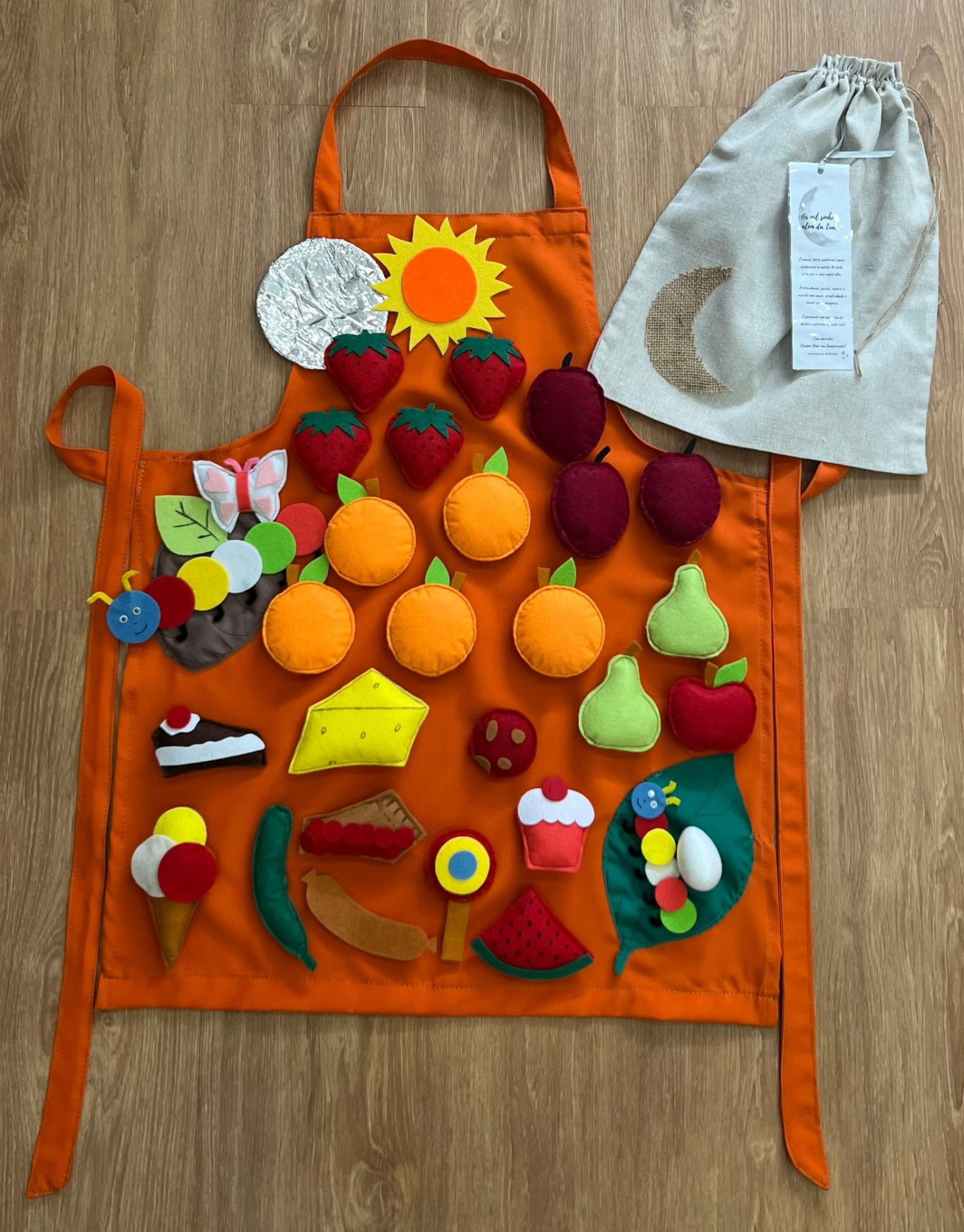 Avental Lagartinha Comilona Avental laranja com peças de alimentos em feltro e saco de pano ao lado