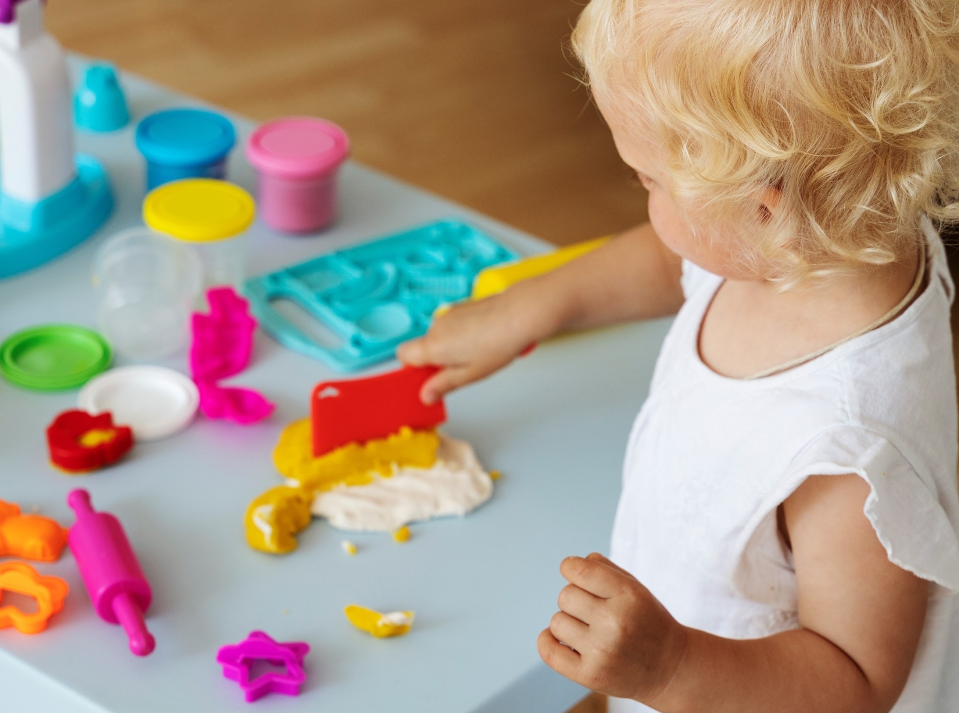 Criança a brincar com massa de modelar e utensílios coloridos numa mesa