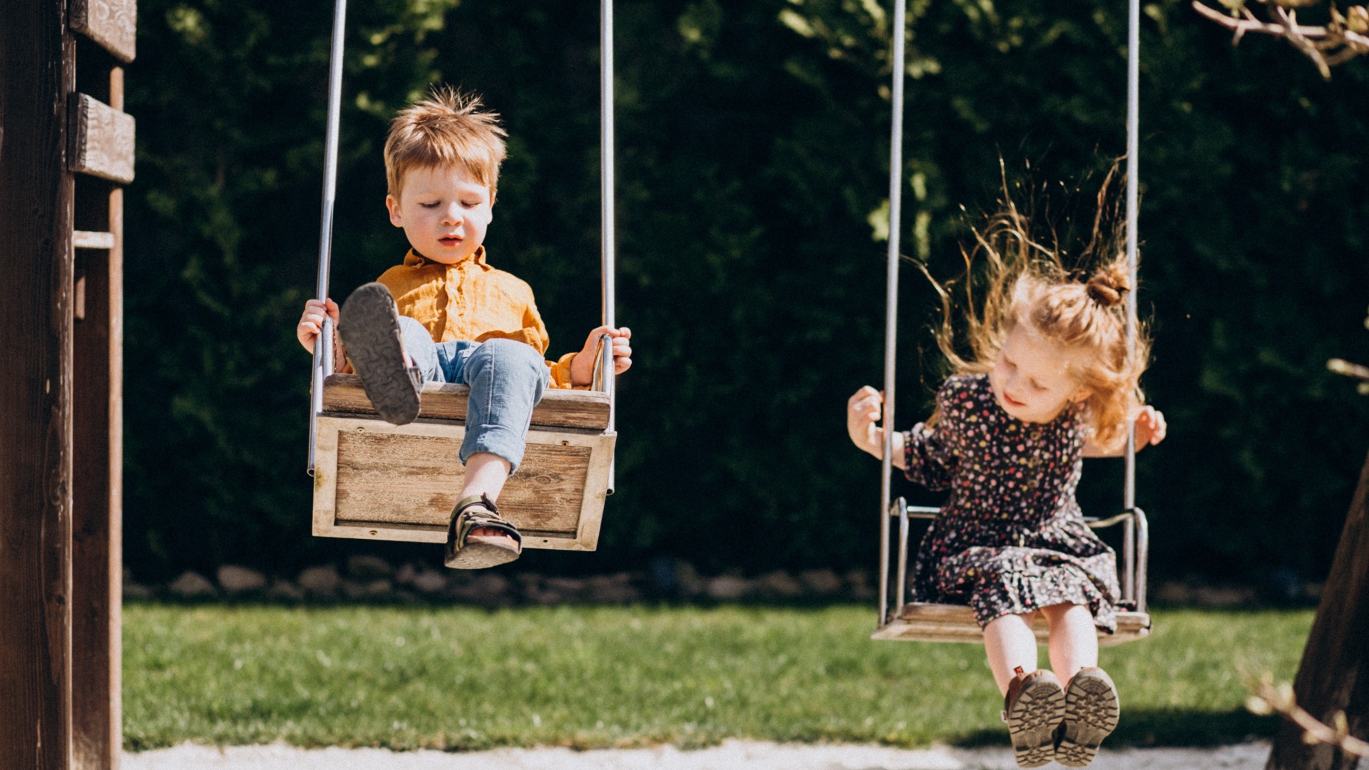 Duas crianças em baloiços de madeira num parque exterior