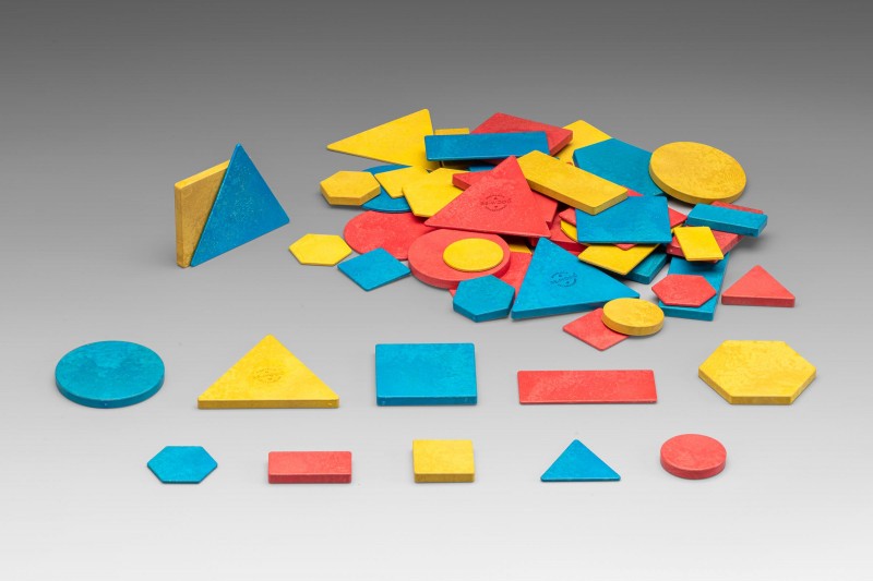 Blocos de atributos Peças geométricas de madeira coloridas em azul, amarelo e vermelho sobre superfície cinzenta