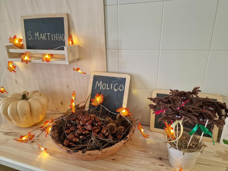 Exposição de S. Martinho com abóbora branca, castanhas em prato de madeira, figura artesanal de castanhas e luzes decorativas em folhas de outono
