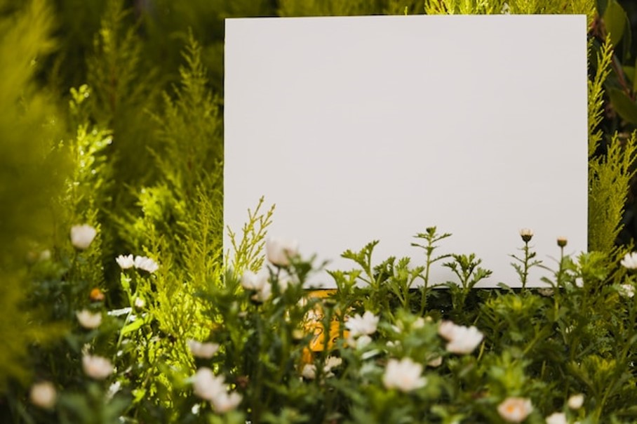 Cartaz branco quadrado rodeado por flores e plantas verdes.
