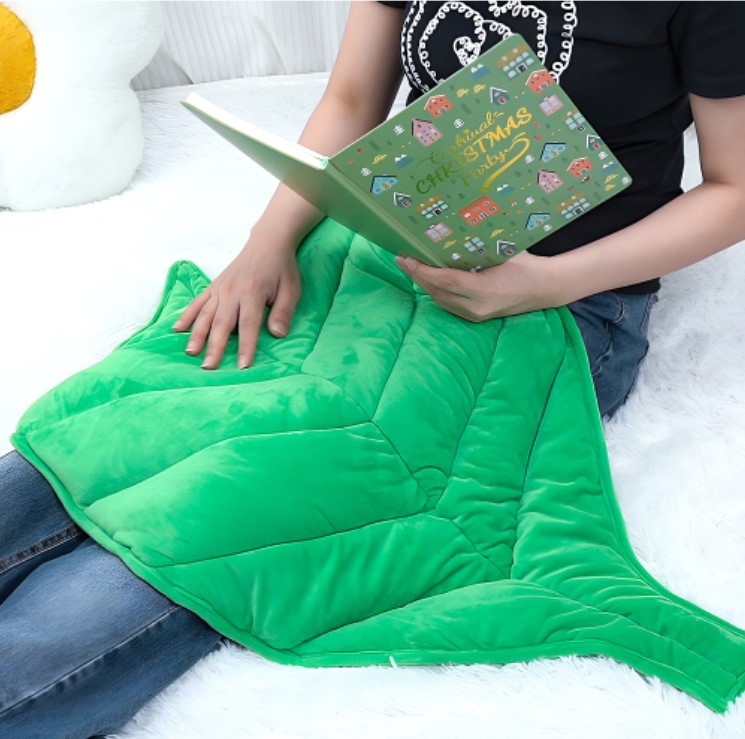 Manta Ponderada Sensorial Folha 2,9 kg Manta verde em forma de folha com pessoa a ler livro verde de Natal