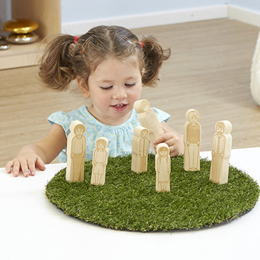 Família de Bonecos de Madeira Menina a brincar com bonecos de madeira sobre tapete verde que imita relva