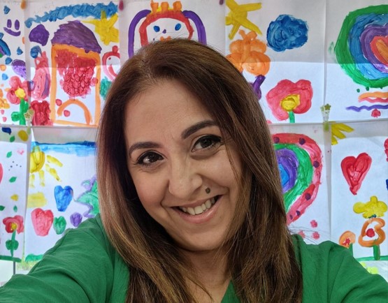 Mulher sorridente em frente a desenhos coloridos de papel