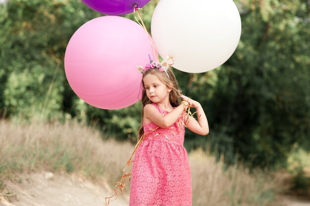 Menina com vestido rosa segurando balões grandes ao ar livre