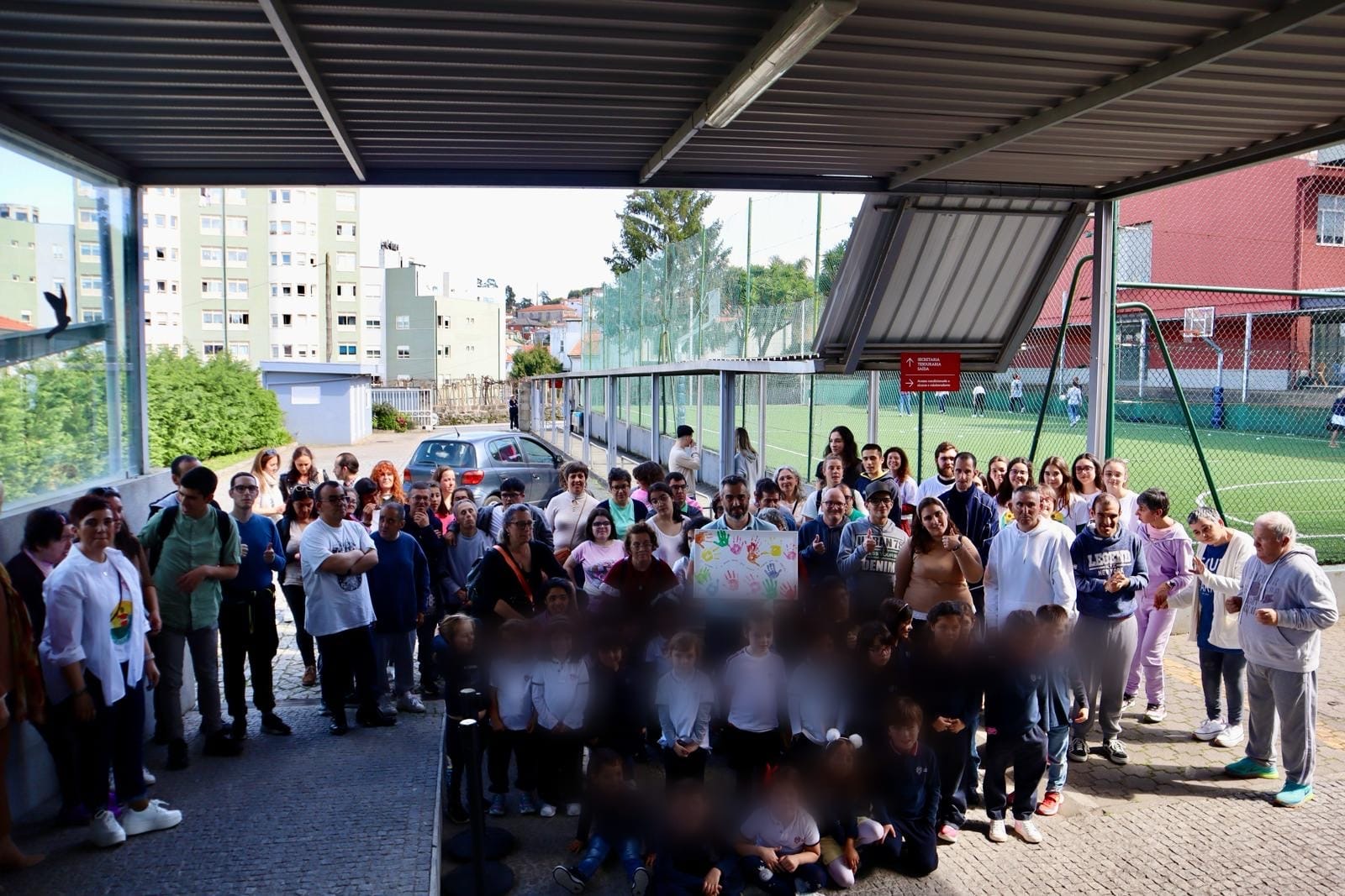Grupo de pessoas em espaço exterior coberto com campo desportivo ao fundo