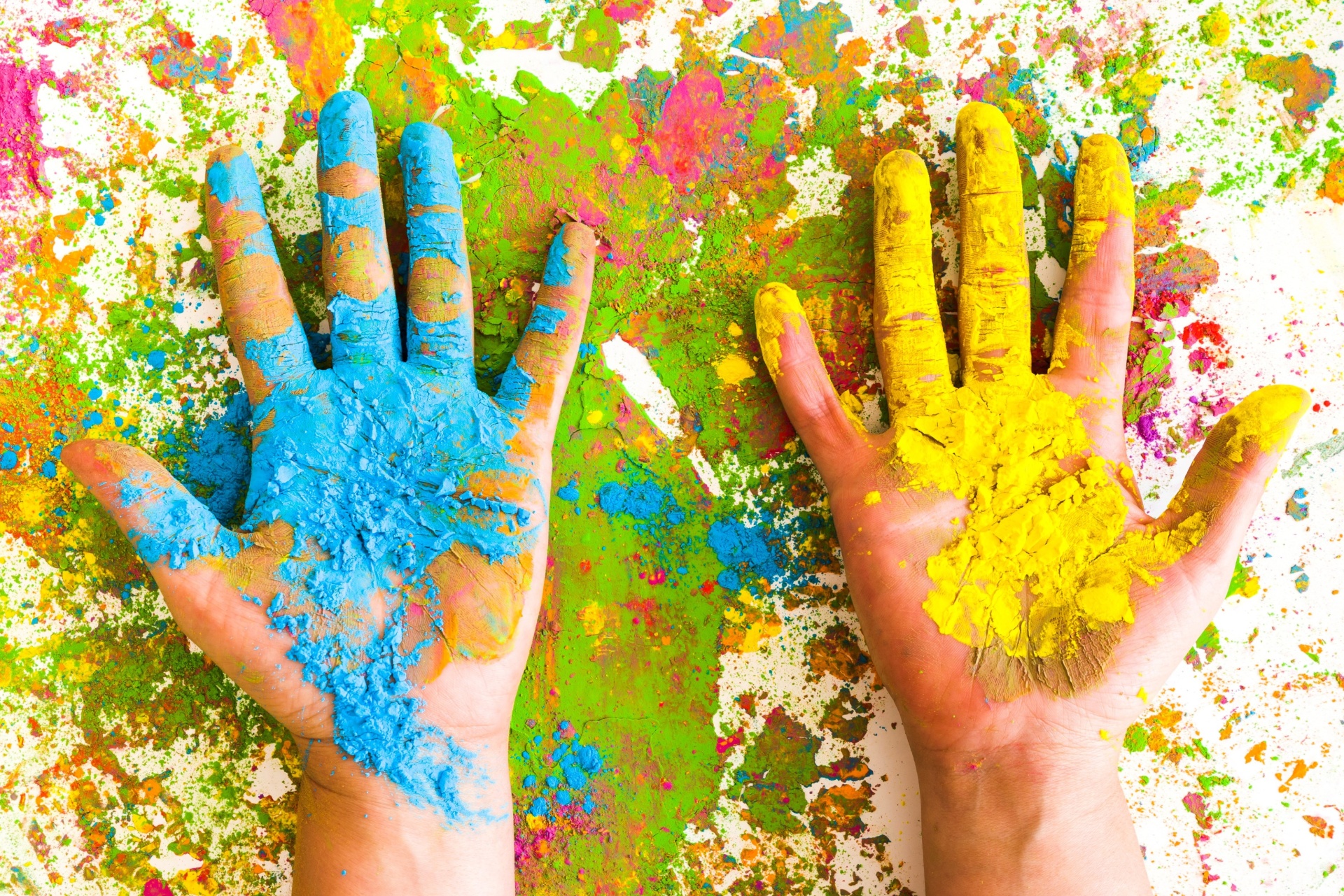 Mãos cobertas de pó colorido azul e amarelo sobre superfície manchada colorida