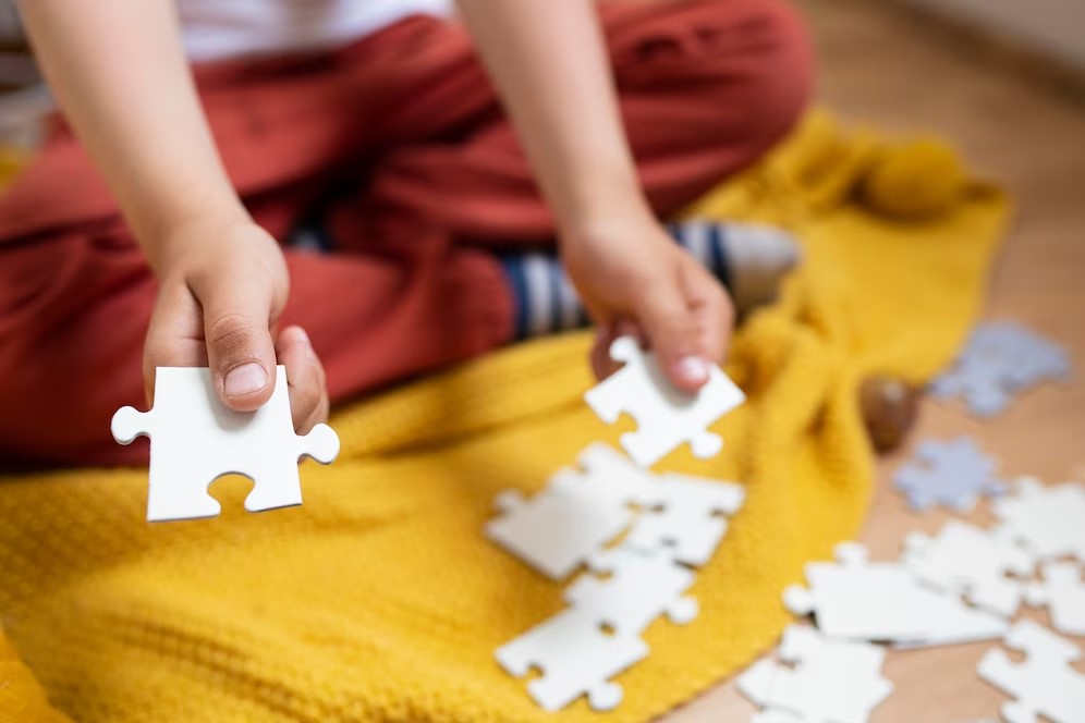Peças de puzzle brancas nas mãos de uma criança sobre tecido amarelo