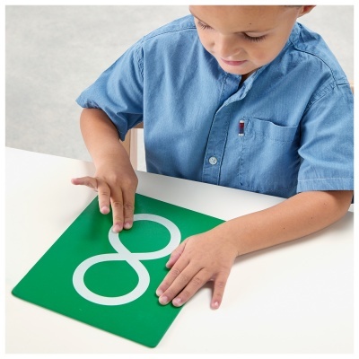 Menino traçando o número 8 tátil numa placa verde