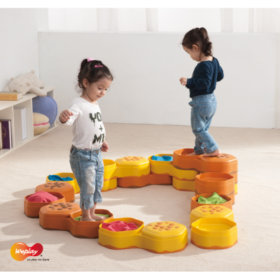 Crianças brincam em tapete modular hexagonal colorido para atividades em espaço interior.